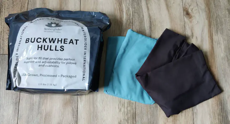 A bag of buckwheat hulls and two pillow cases laid out on a wood floor