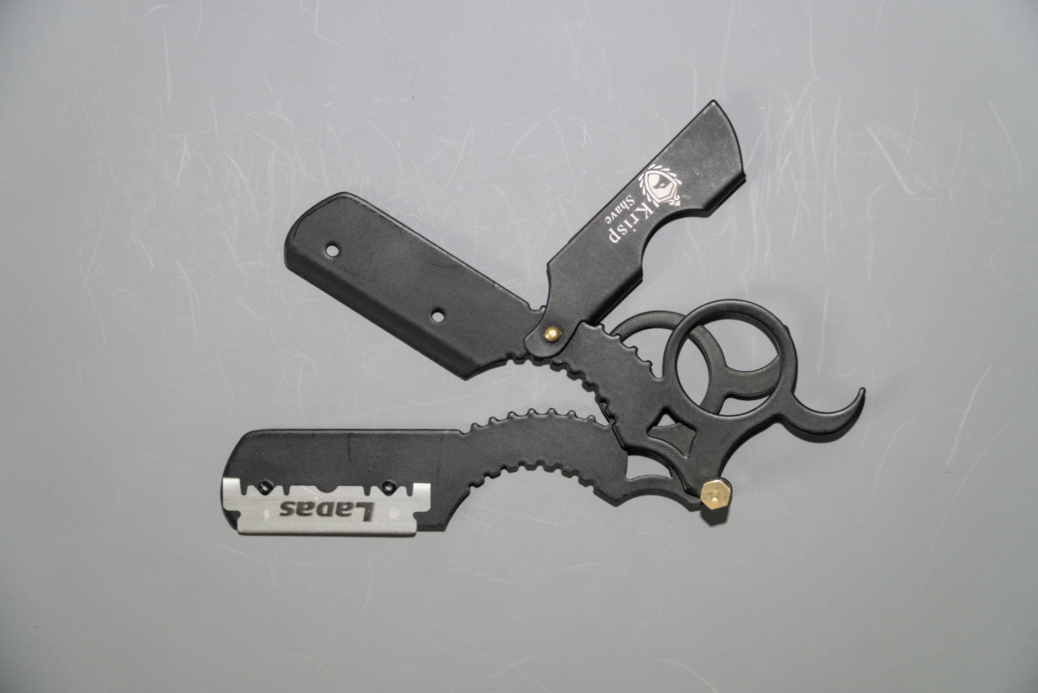 A mini straight razor with swappable blade and finger ring pulled apart to show how the swappable blade feature works