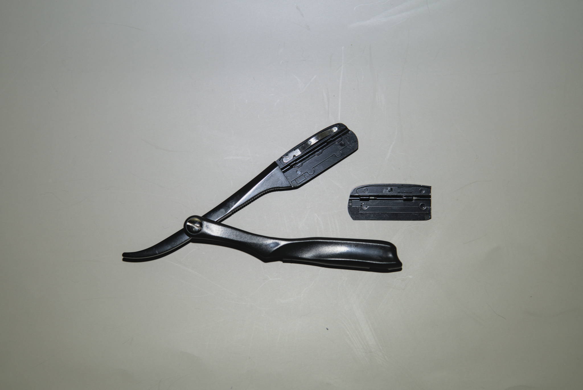 A swappable blade, folding straight razor with the blade compartment open & parts shown