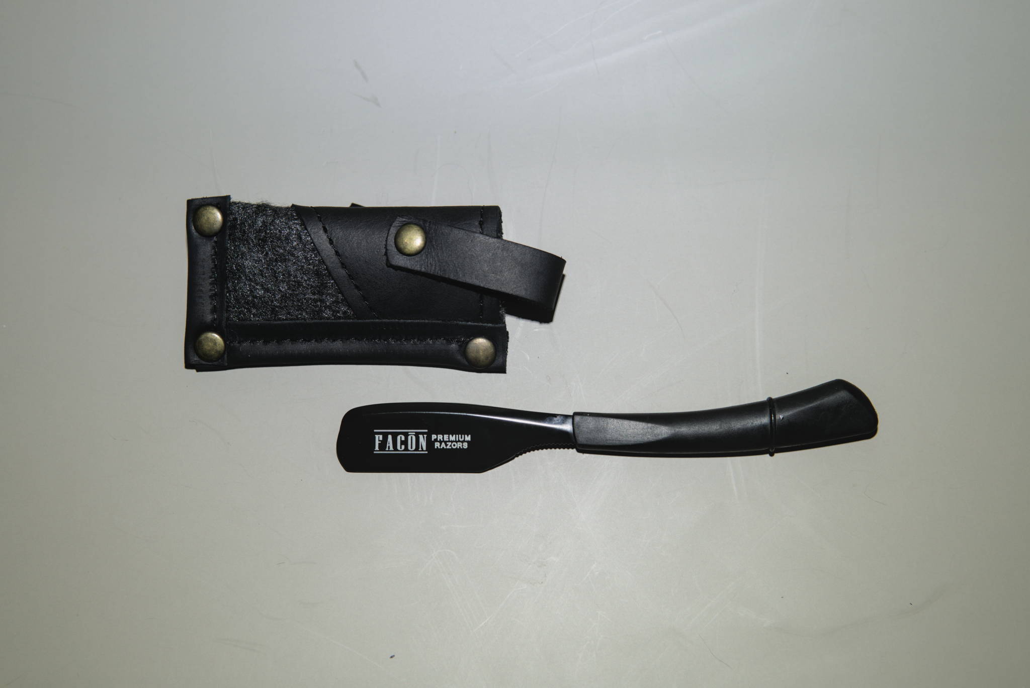 A swappable blade, fixed handle straight razor next to its case